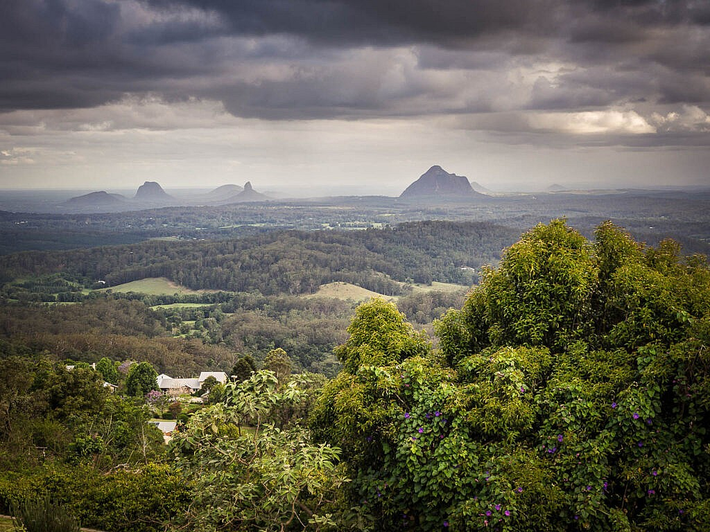 View of the Glass House Mountains peaks under a moody, overcast sky from a hinterland lookout.