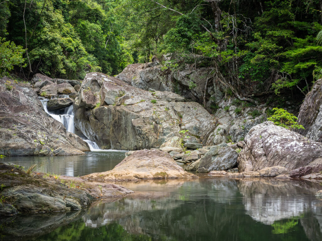 View of a waterfall flowing over large boulders into a clear rock pool, located past Artists Cascades within Conondale National Park, Sunshine Coast.