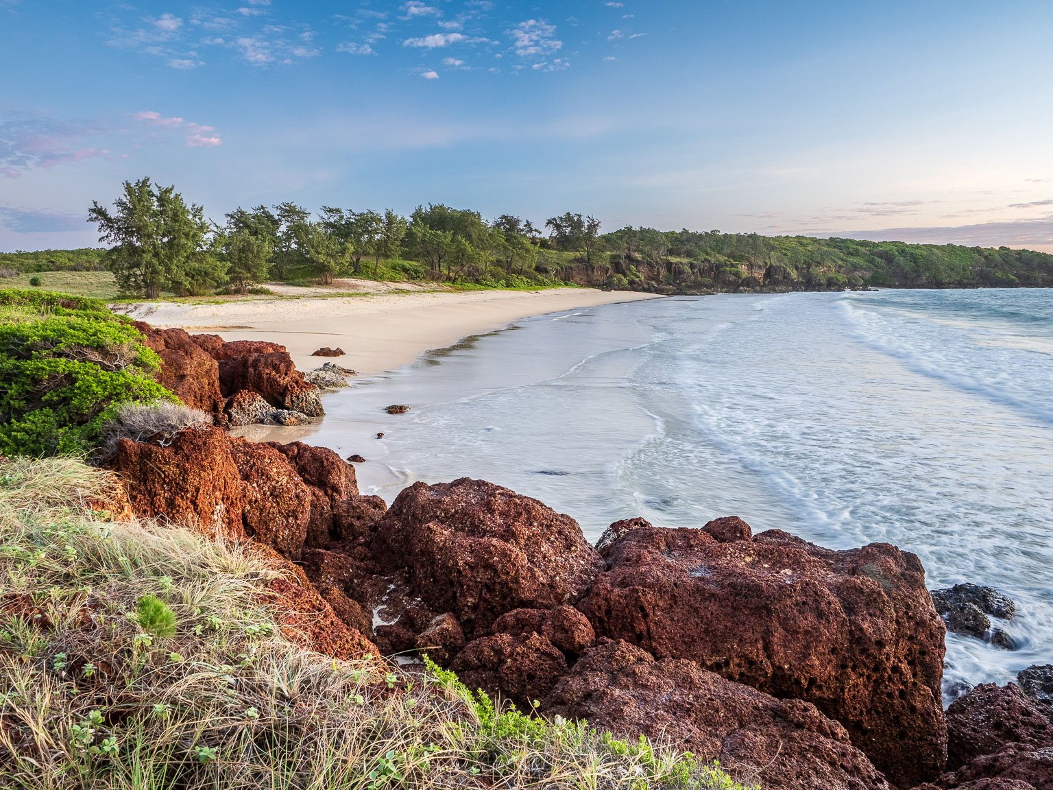 Sunrise over the red volcanic rock shelves, white sand and calm ocean waters at Macassan Beach in East Arnhem Land.