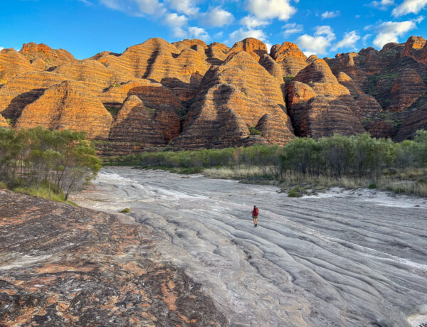 A hiker walks across the unique rocky landscape of Purnululu National Park (the Bungle Bungles) in Australia. Fully geared for a multi-day trek against a backdrop of massive, beehive-like domes. This image highlights the equipment needed for challenging environments, as discussed in the post.