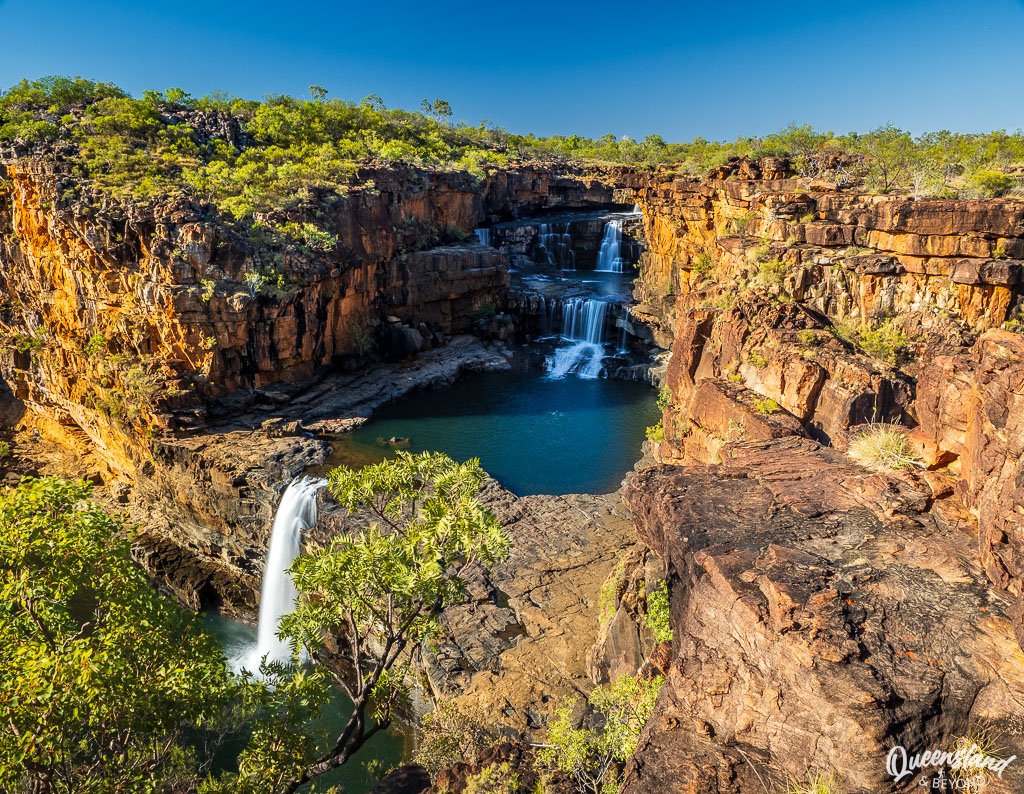 A spectacular wide shot of the four-tiered Mitchell Falls cascading into deep pools surrounded by rugged red sandstone cliffs in the Kimberley.