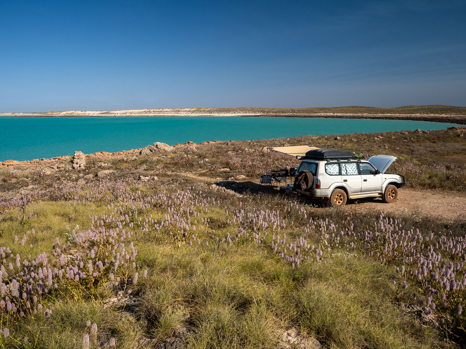 A white 4WD with a rooftop tent set up on the edge of a rugged, limestone cliff overlooking the turquoise ocean at Cape Keraudren in Western Australia.